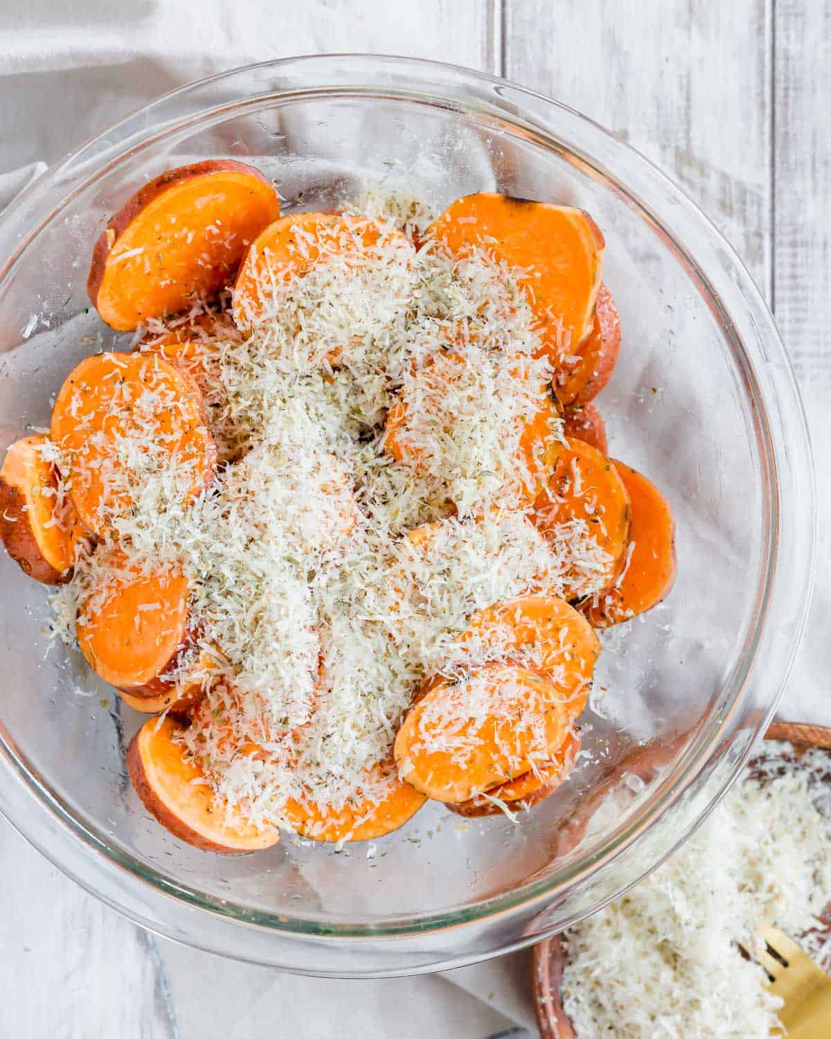 Sliced sweet potatoes with a parmesan herb mixture in a glass bowl.