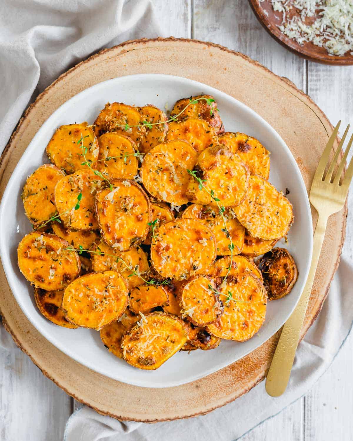 Air fryer sweet potatoes served with fresh thyme sprigs on a white ceramic plate with a serving fork on the side.