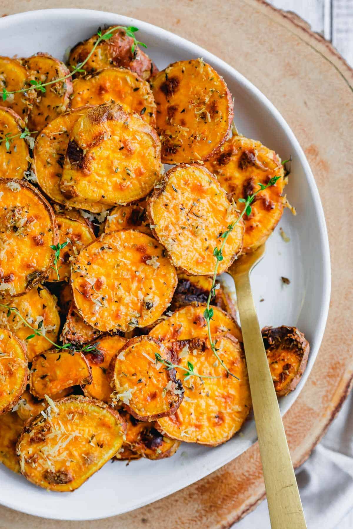 Air fryer sweet potatoes with sprigs of thyme on a serving plate with a gold fork.