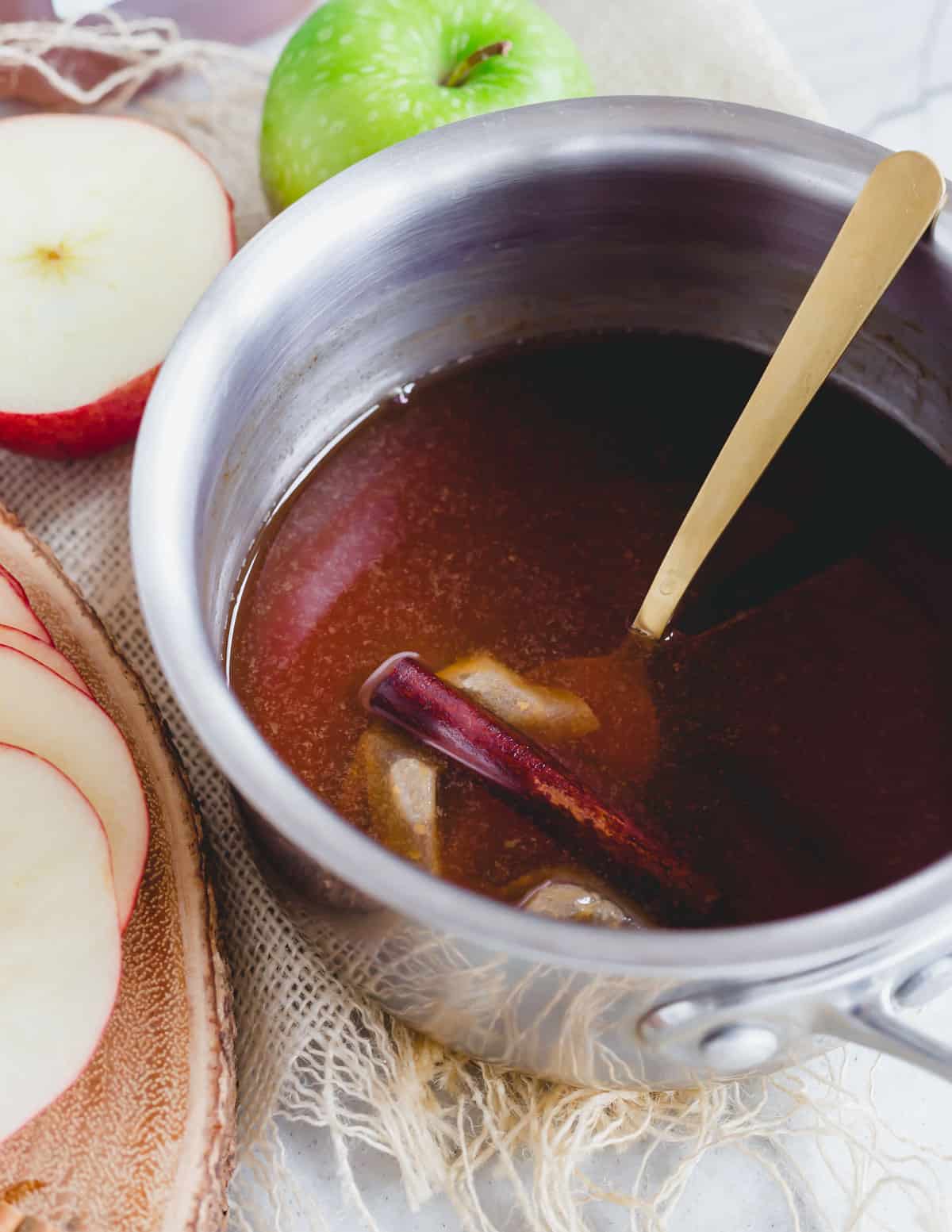 Black tea bags simmering with apple cider in a metal pot with a cinnamon stick.