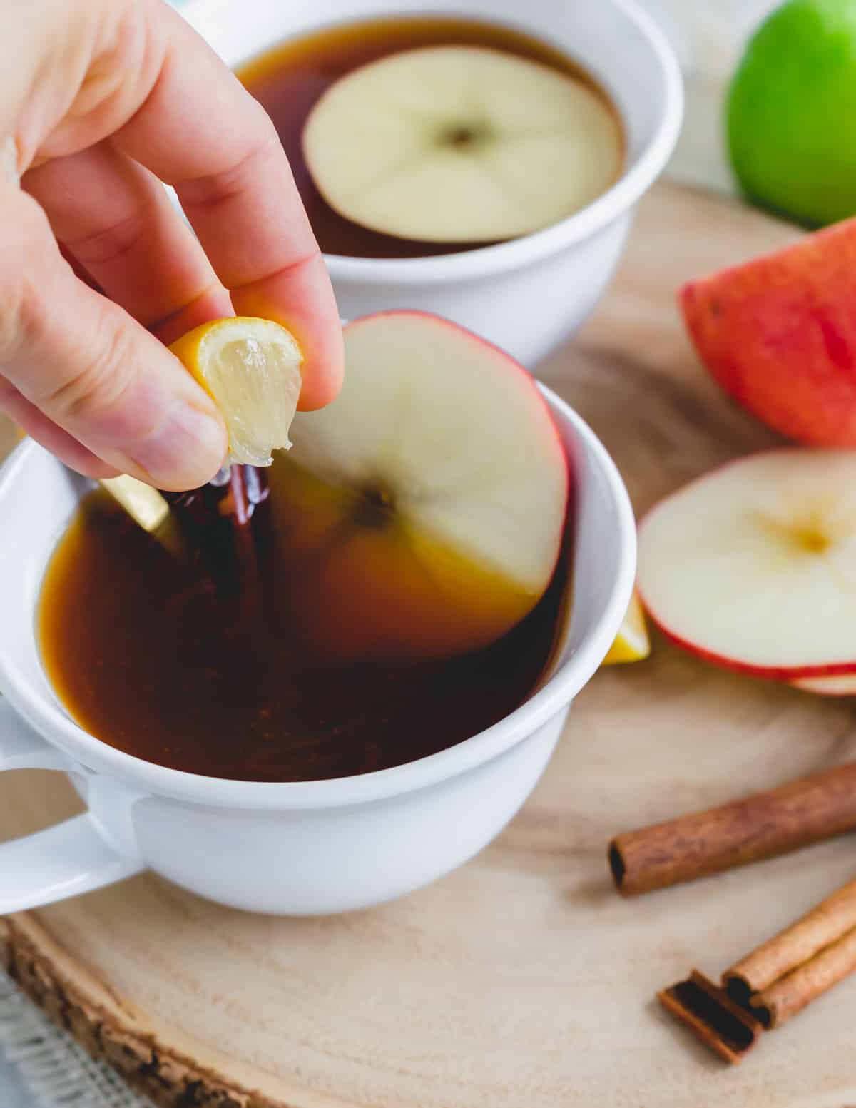 Squeezing a lemon wedge into apple cider tea in a white mug.