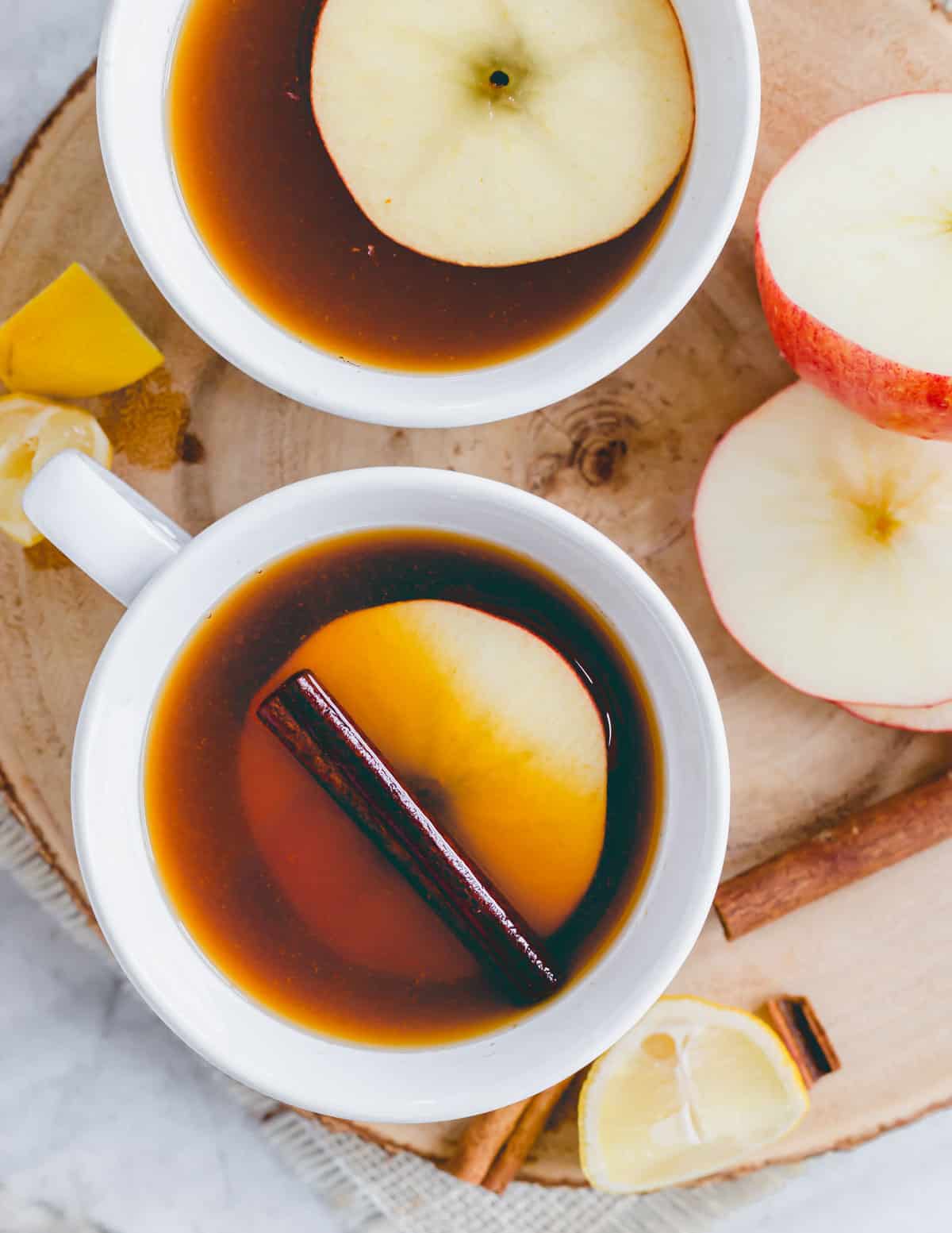 Non-alcoholic warm apple cider black tea with a cinnamon stick and round apple slice in a white mug.