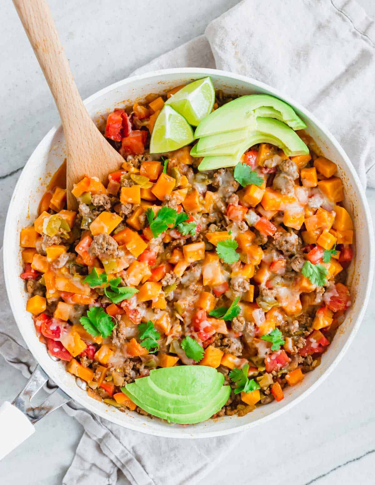 Overhead shot of Tex-Mex flavored ground beef and sweet potato skillet with a wood serving spatula and sliced avocado and lime.