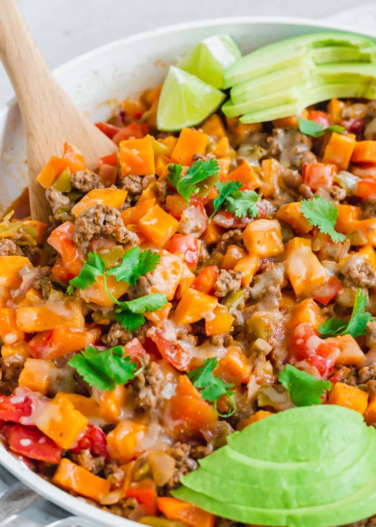 Southwest ground beef and sweet potato recipe in a white skillet with a wooden spatula.