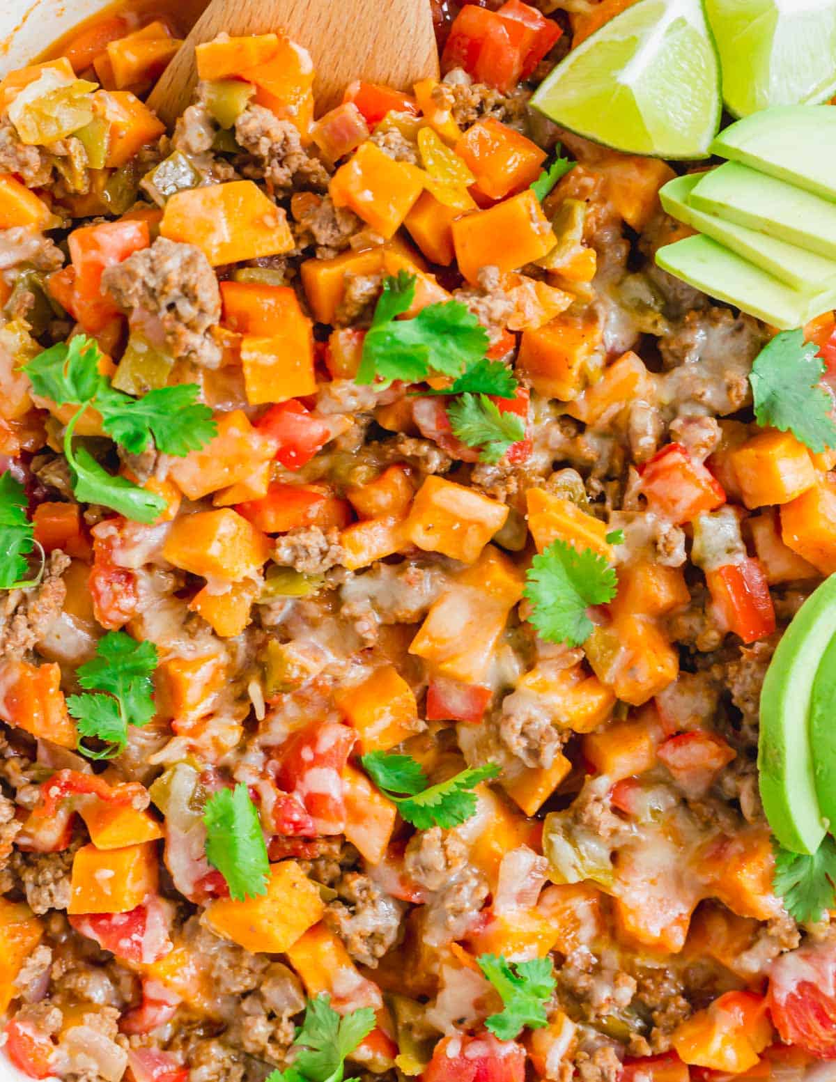 Sweet potato and ground beef recipe with peppers, onions, tomatoes and cheddar garnished with fresh cilantro and avocado slices.