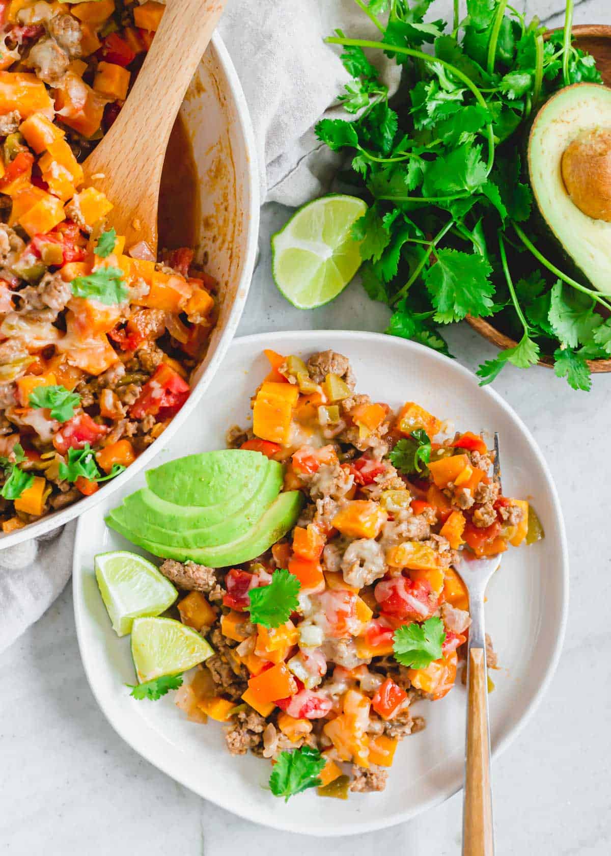 A serving of ground beef and sweet potato skillet recipe on a white plate with a fork.