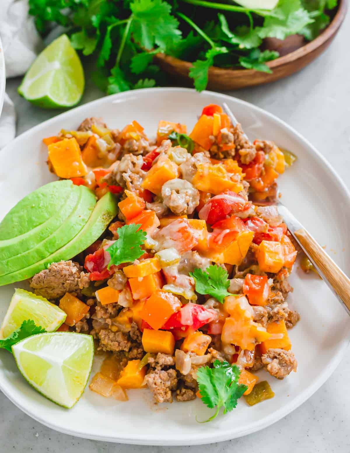 Easy recipe for ground beef with sweet potatoes served on a plate with lime quarters and sliced avocado.