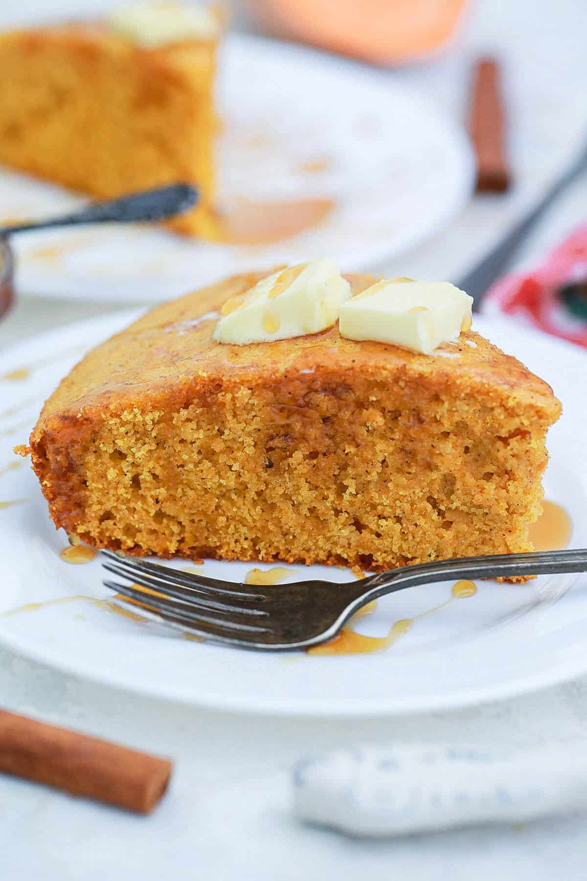 Southern sweet potato cornbread slice on a white plate with a fork and two pats of butter on top.