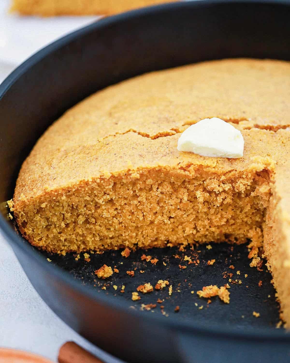 Sweet potato cornbread in a cast iron skillet with a pat of butter on top.