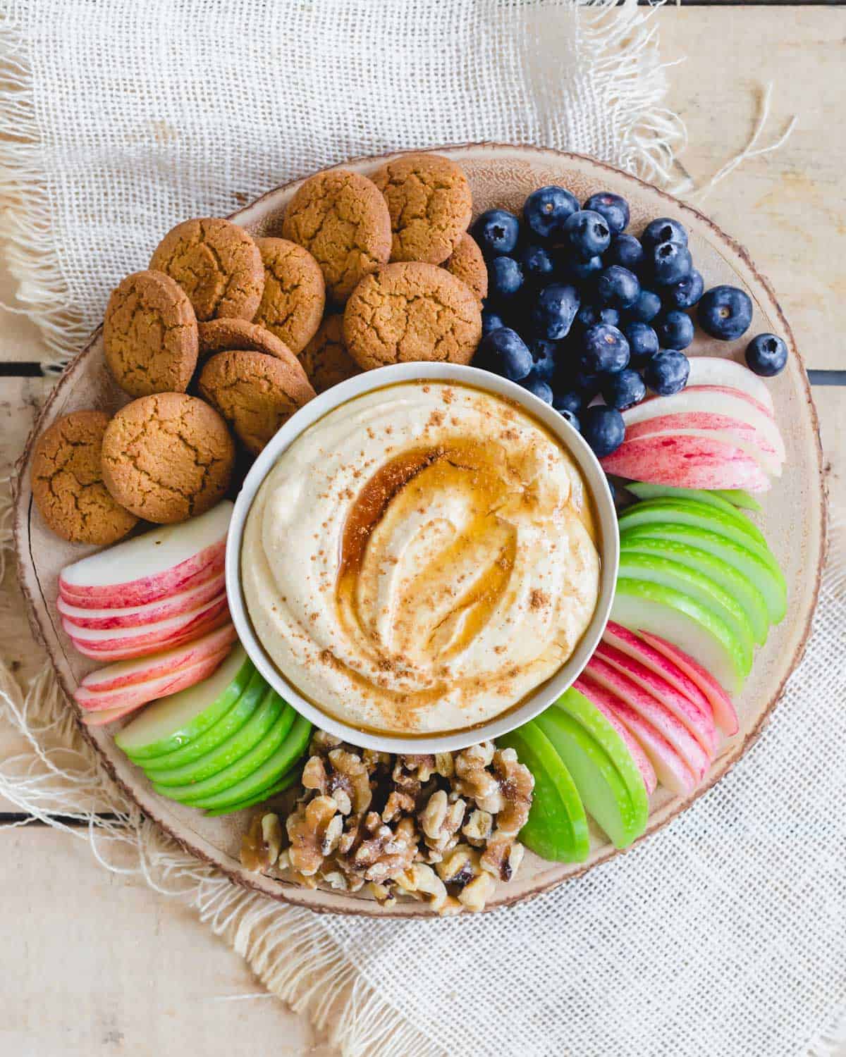 Pumpkin ricotta dip with maple syrup and pumpkin pie spice in a serving bowl on a wood board with dippers around it.