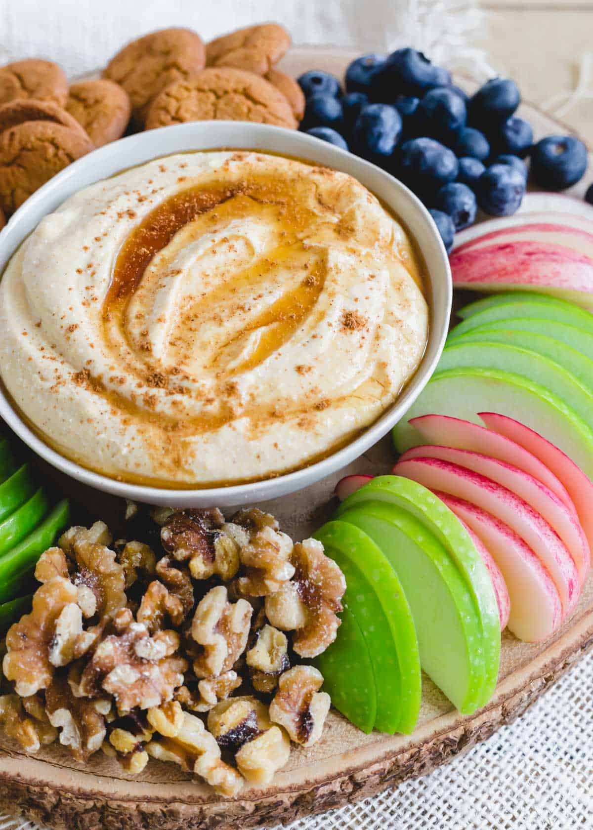 Whipped ricotta dessert dip in a small bowl served with apple slices, walnuts, gingersnaps and blueberries.