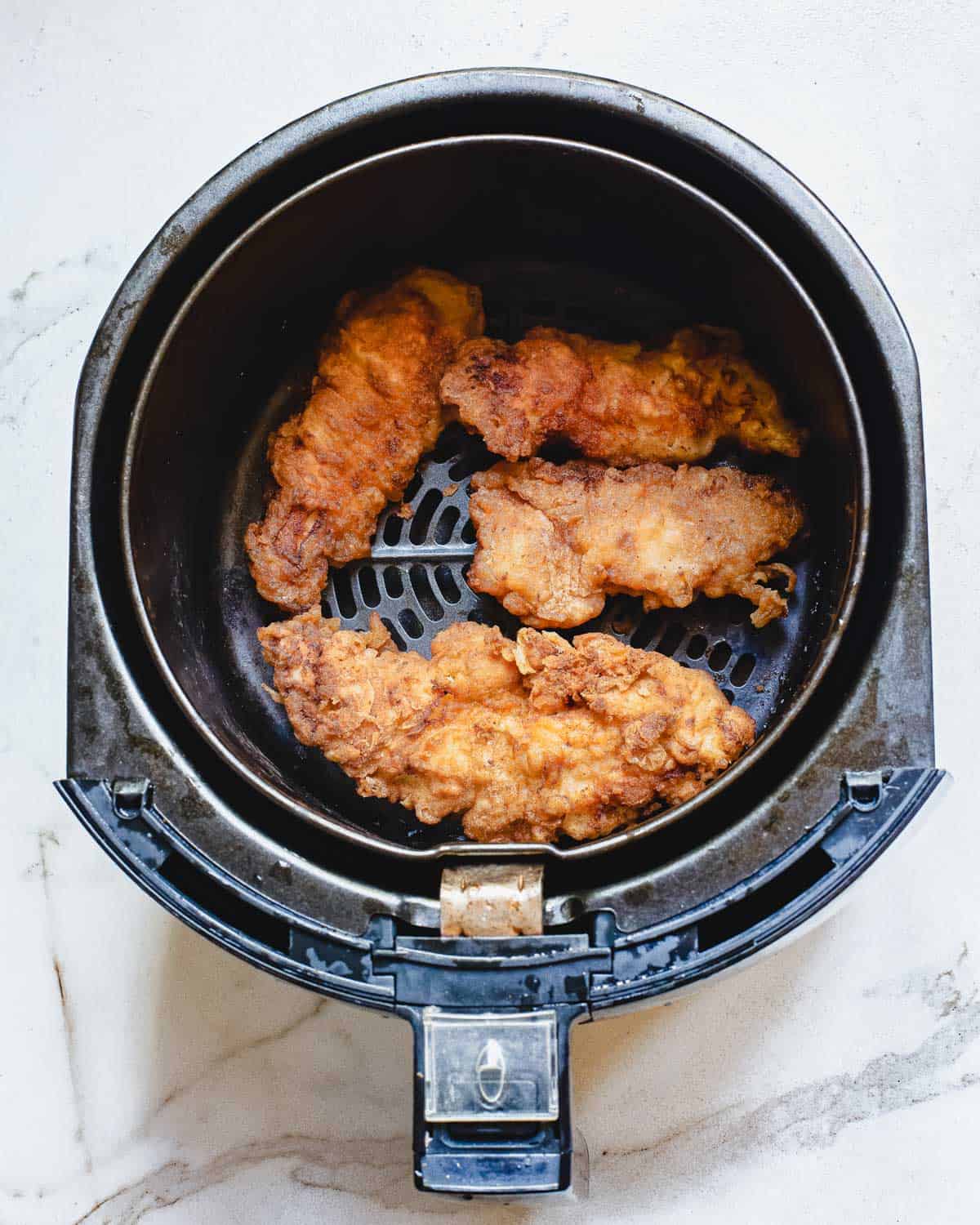 Crispy chicken tenders in an air fryer basket.