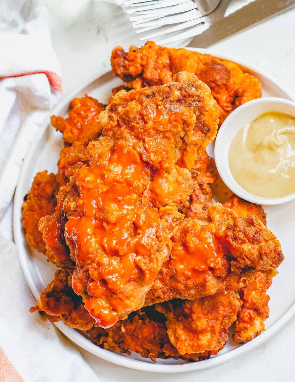 Crispy buffalo chicken cooked in the air fryer on a plate with a dipping sauce on the side.