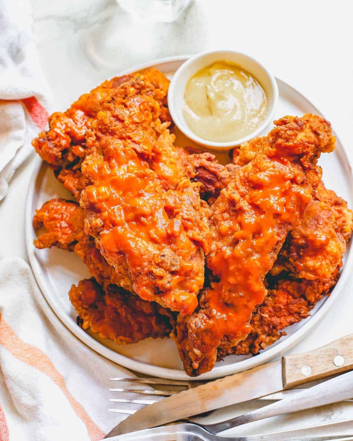 Air fryer buffalo chicken tenders on a white plate with dipping sauce in a small bowl.