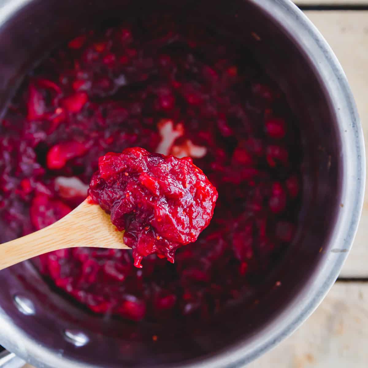 A wooden spoon with cranberry jam over a pot.