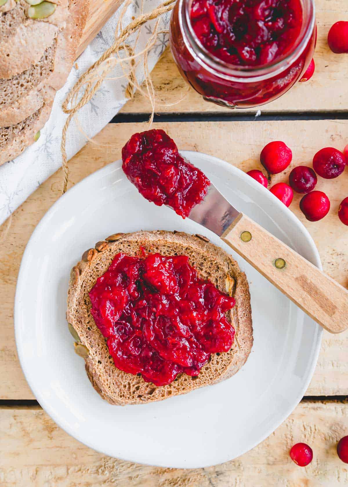 Cranberry ginger jam spread on a piece of toast on a plate.