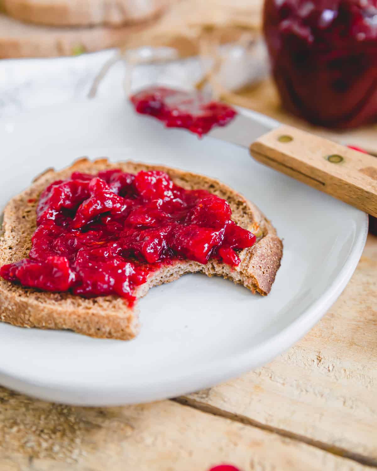 Cranberry jam spread on a piece of toasted sourdough bread on a plate.