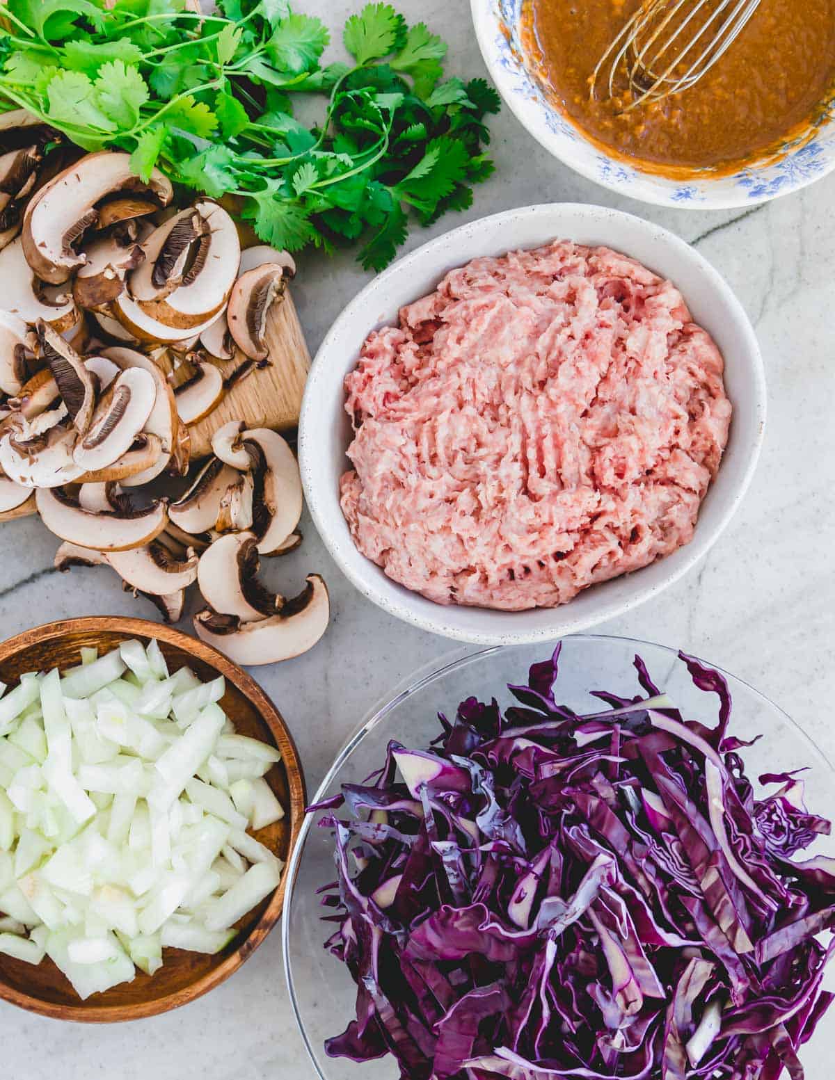 Ingredients to make a pork and cabbage skillet recipe including ground pork, sliced red cabbage, sliced mushrooms, chopped onion and an Asian stir fry sauce.