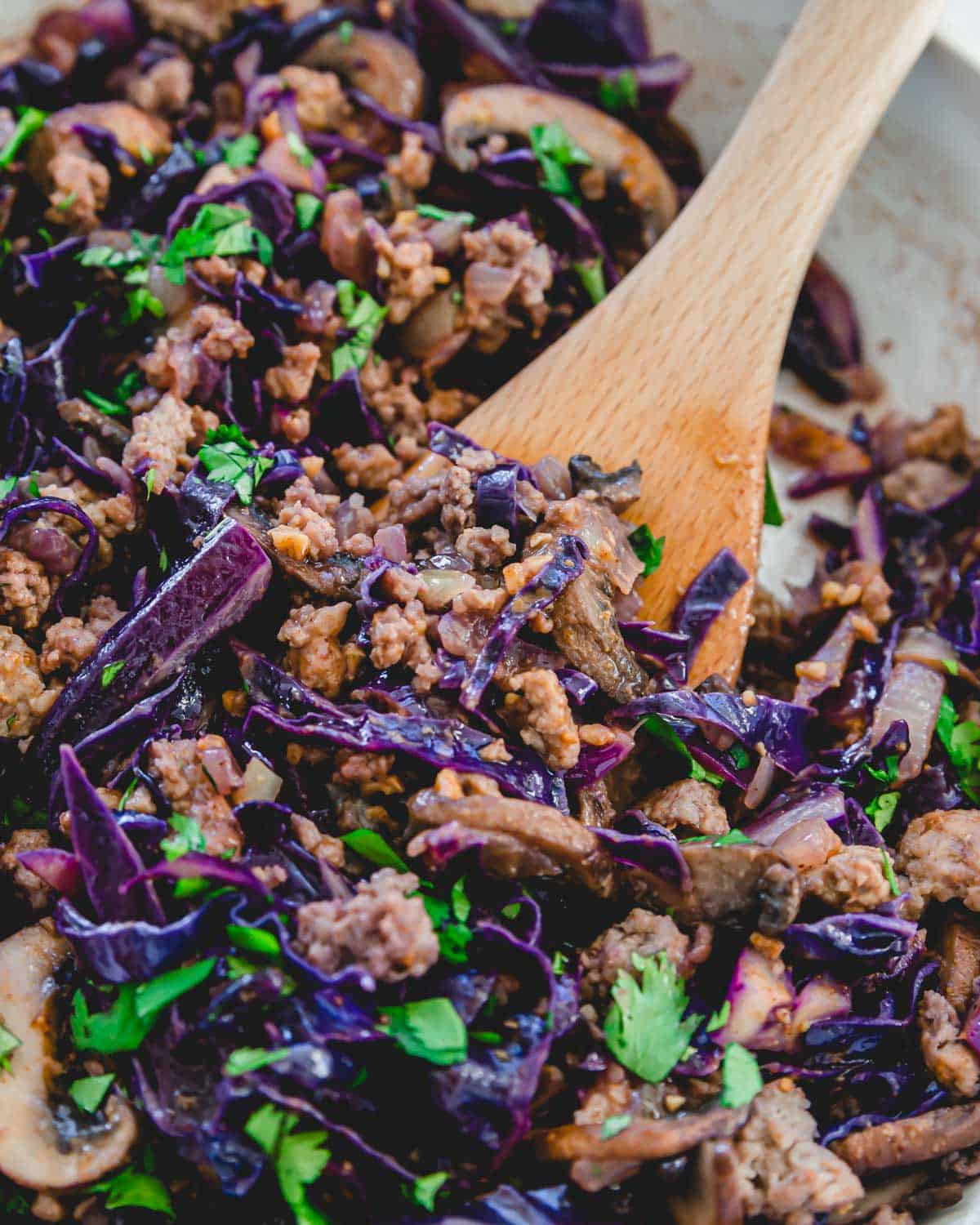 Ground pork and cabbage recipe in a skillet with a wooden spatula.