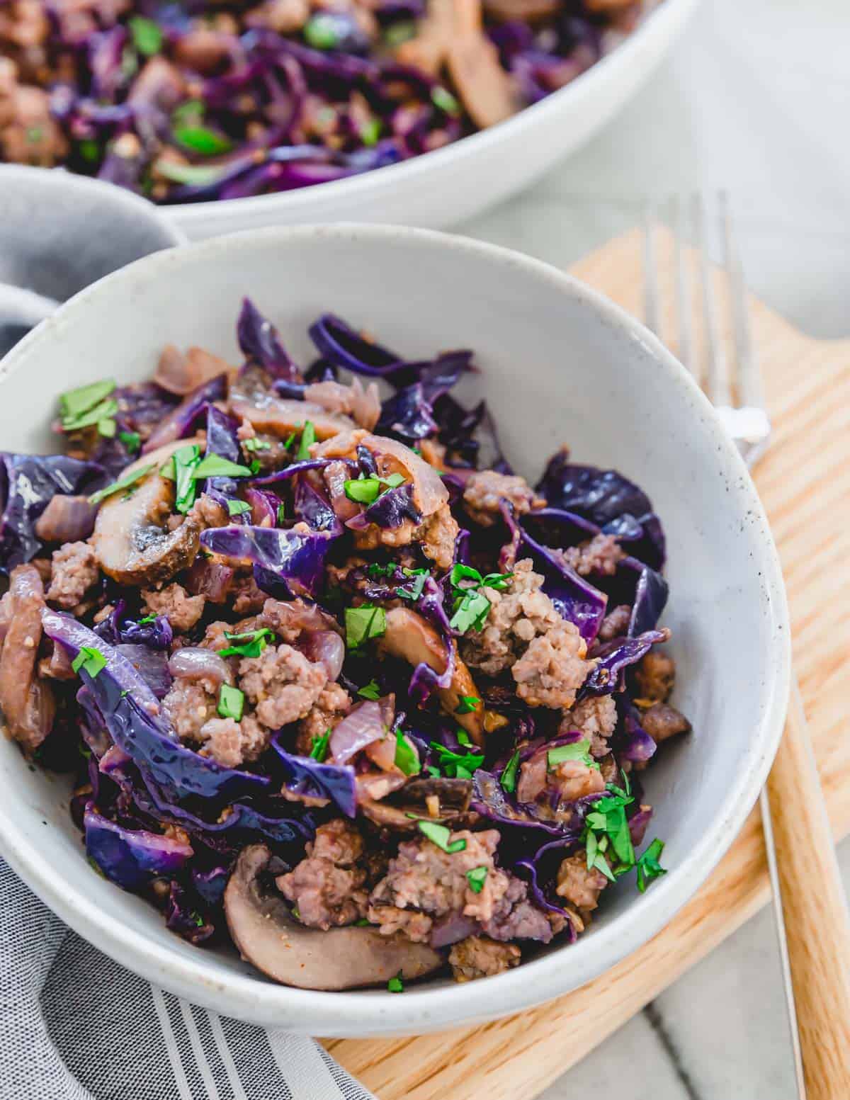 Pork and cabbage stir fry in a ceramic bowl on a cutting board.