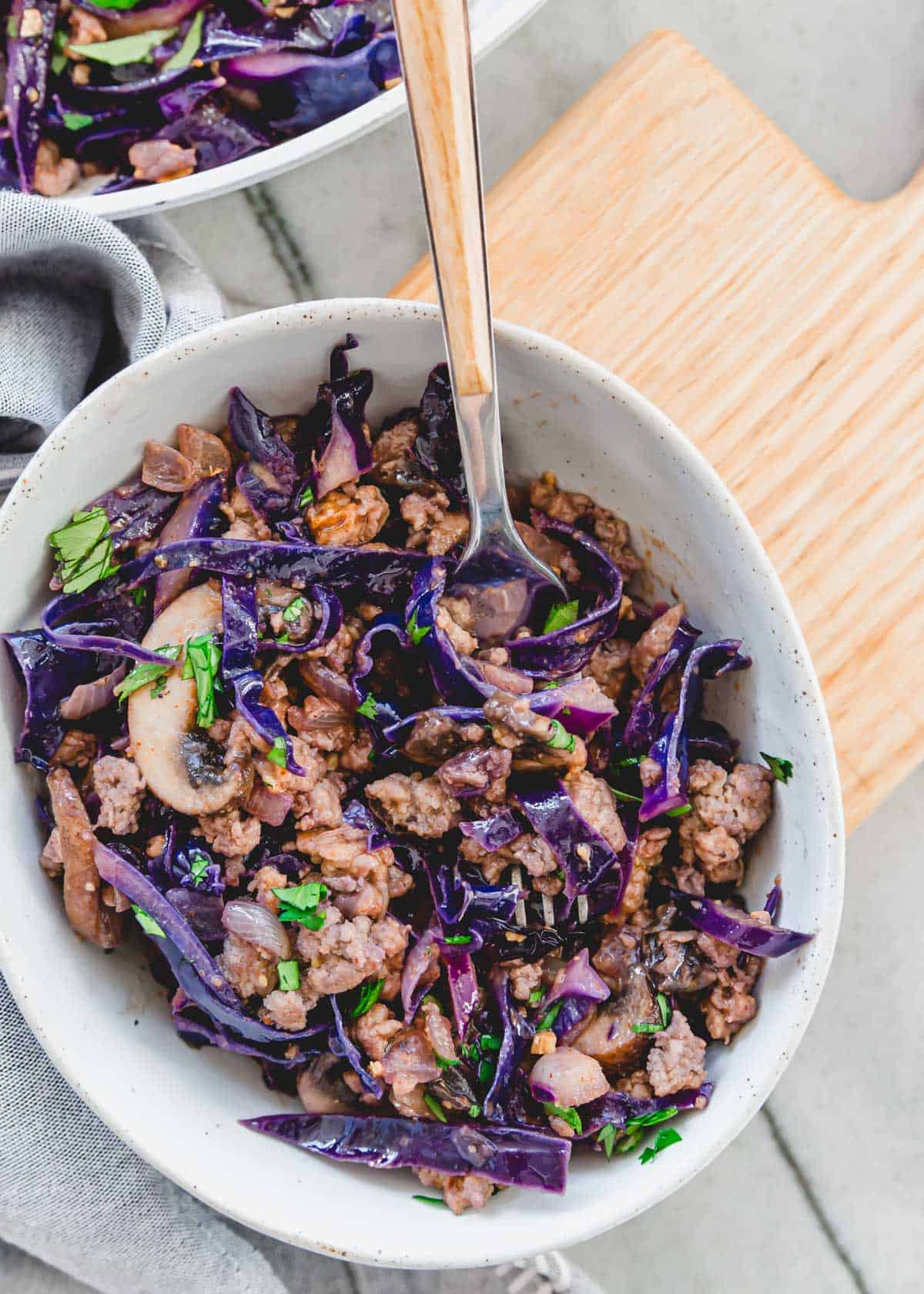 Ground pork and cabbage stir fry recipe with mushrooms in a bowl with a fork.