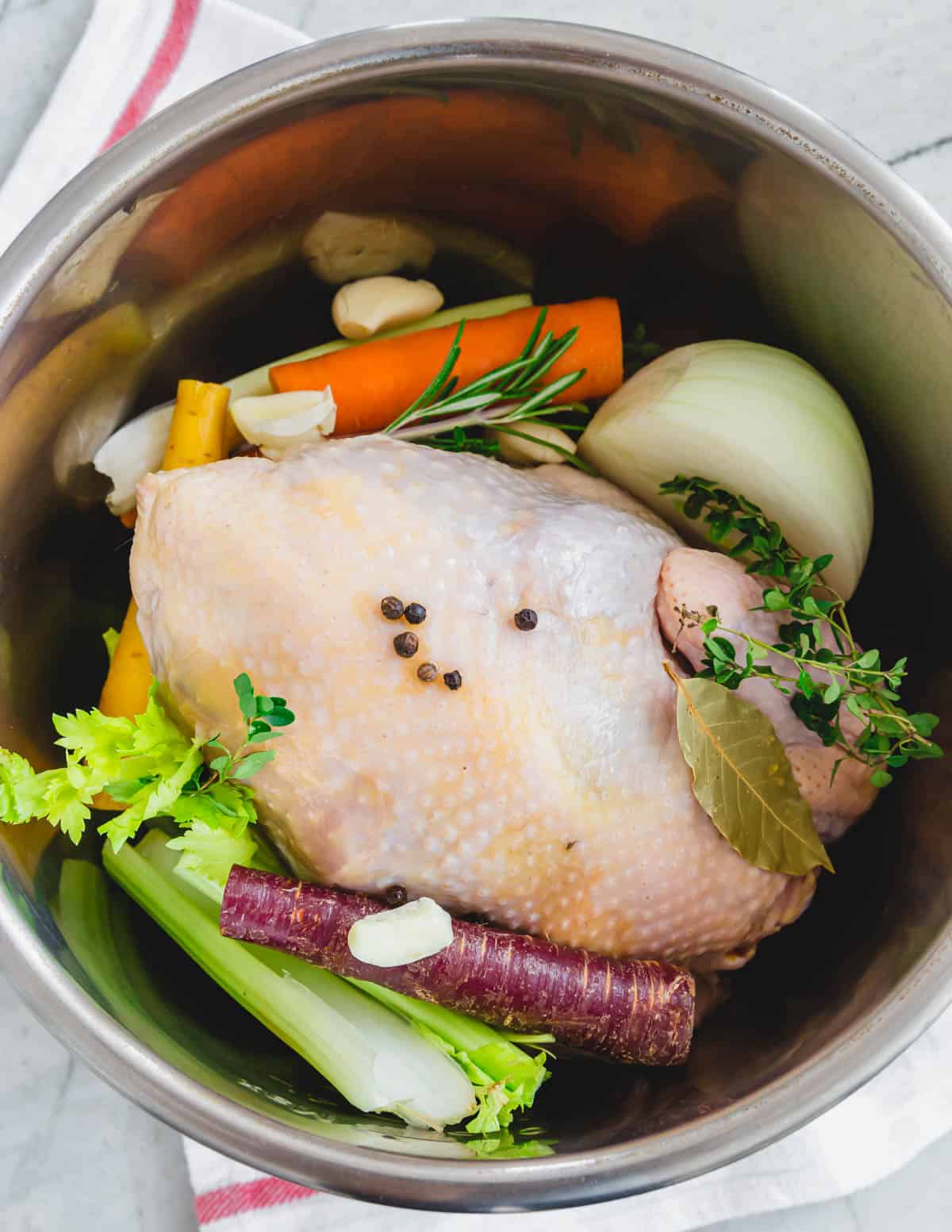 Stewing hen in the insert of an Instant Pot with vegetables.