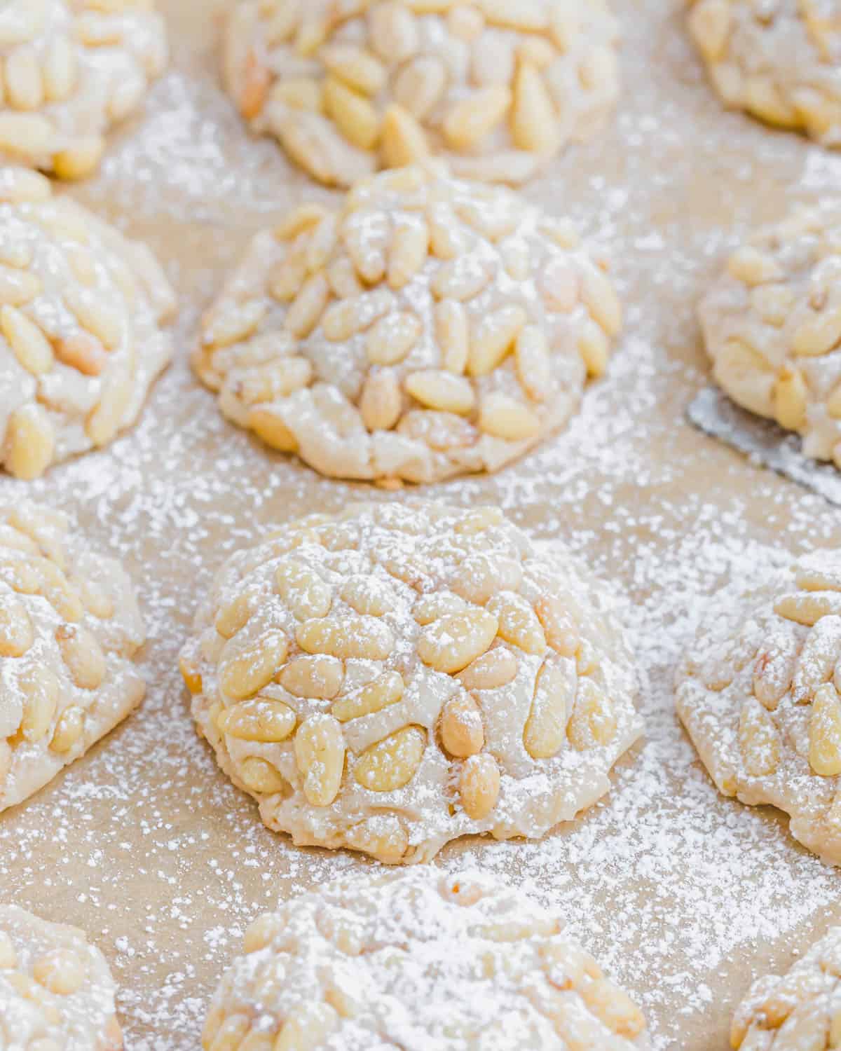 Pignoli cookies on a baking sheet dusted with powdered sugar.