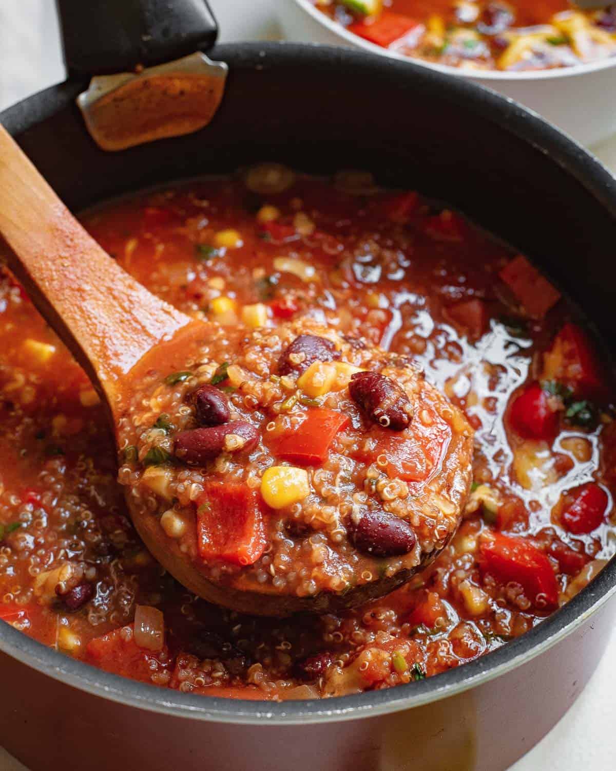 Vegetarian Mexican soup with quinoa in a pot with a wooden spoon.