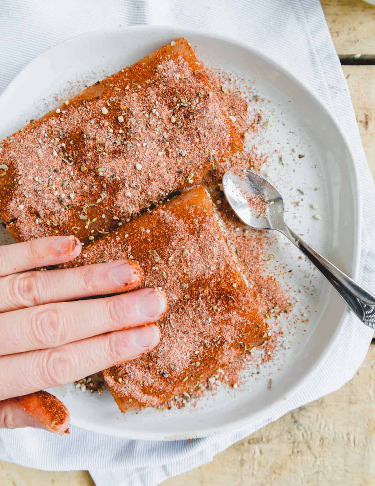 Pressing blackening seasoning onto mahi mahi filets on a plate.