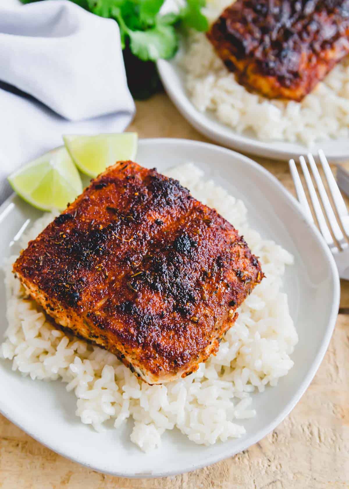 Blackened mahi mahi filet over white rice on a plate.