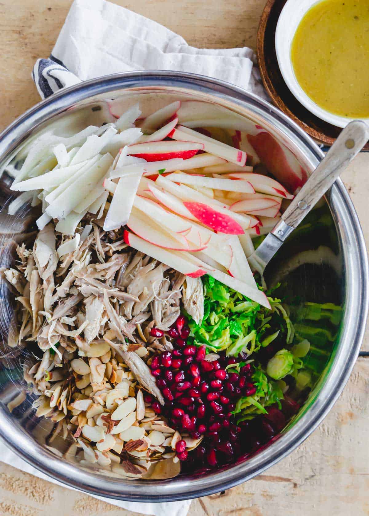 Tossing chicken and shredded Brussels sprouts salad together in a metal bowl with a wooden spoon.