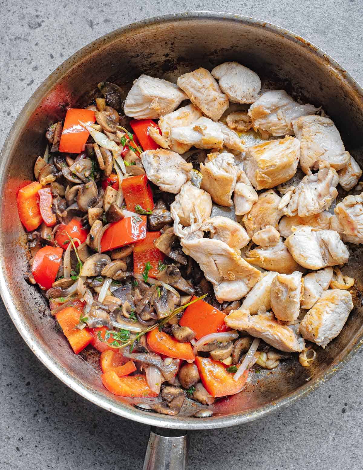 Chicken bites in a pan with mushrooms, onions and peppers on the side.