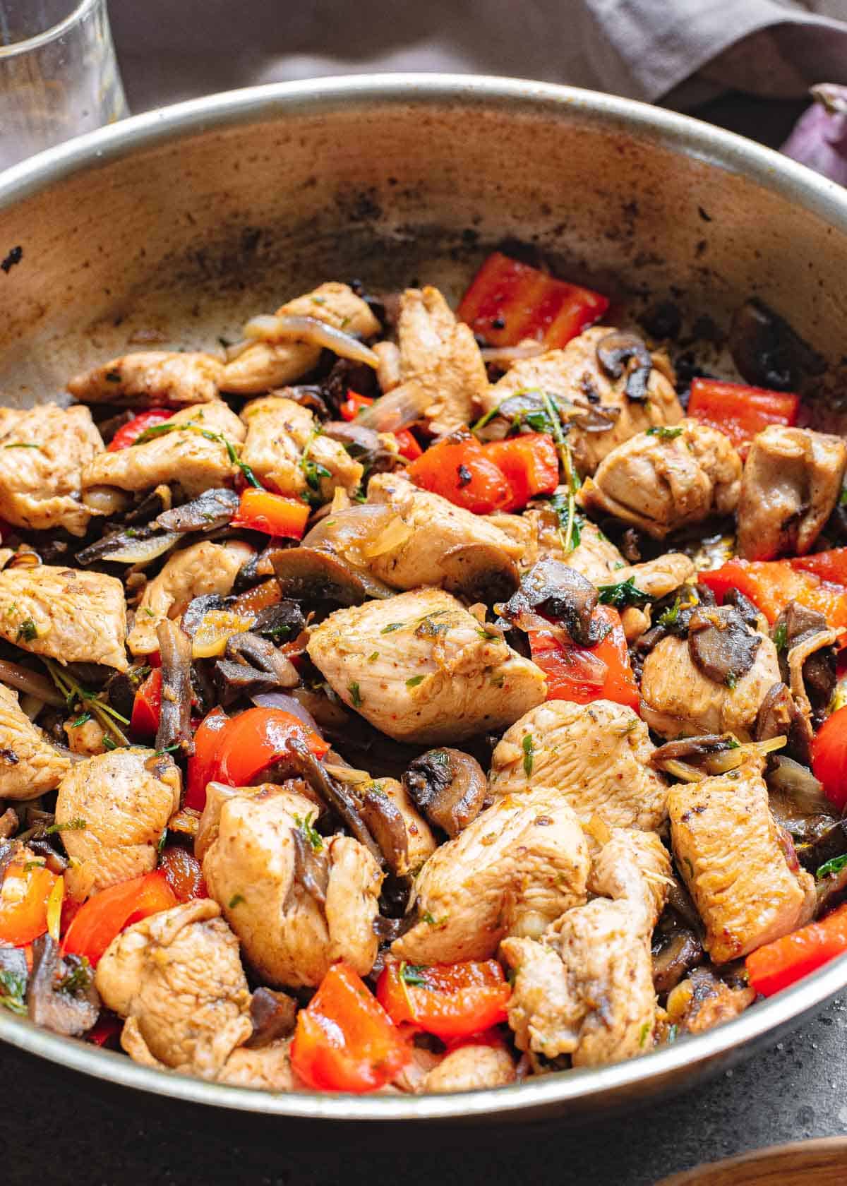 Garlic chicken bites in a stainless steel skillet with red peppers, mushrooms and onions.