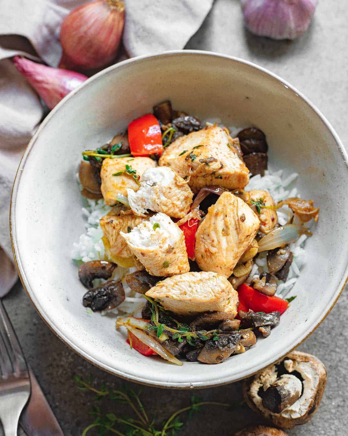 Chicken bites in a bowl served over rice with vegetables and herbs.