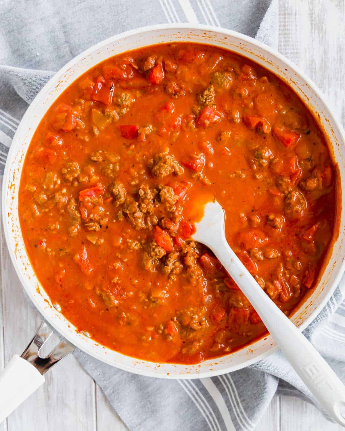 Ground beef with a chunky tomato sauce in a white skillet with spatula.
