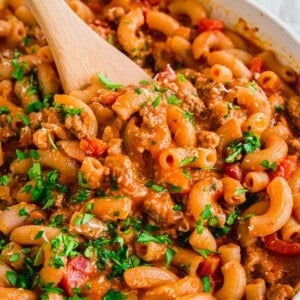 Ground beef with pasta in a skillet with wooden spoon.
