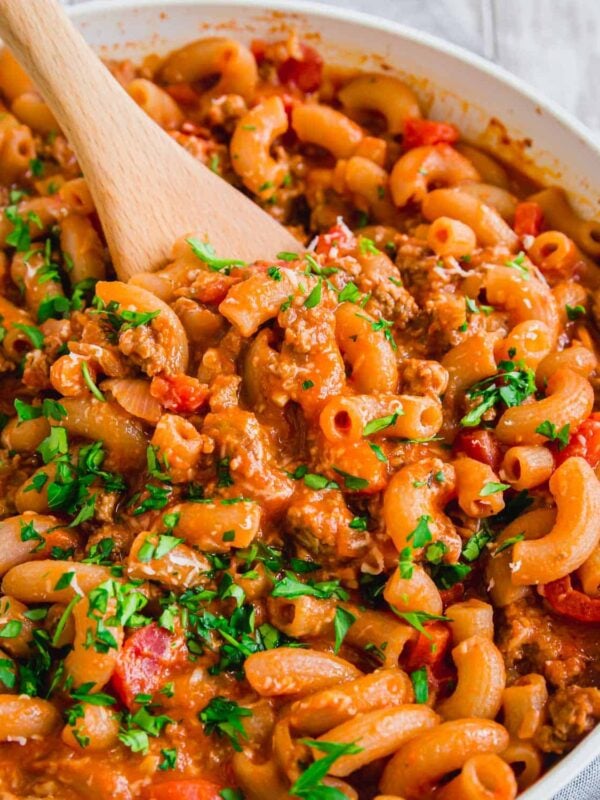 Ground beef with pasta in a skillet with wooden spoon.