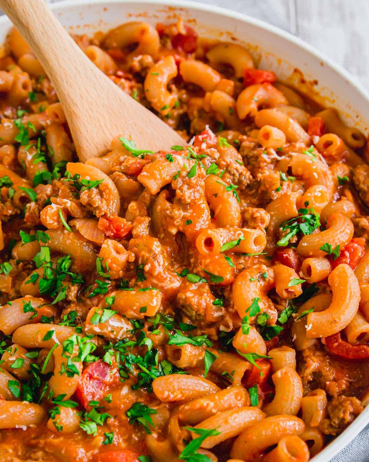 Ground beef with pasta in a skillet with wooden spoon.