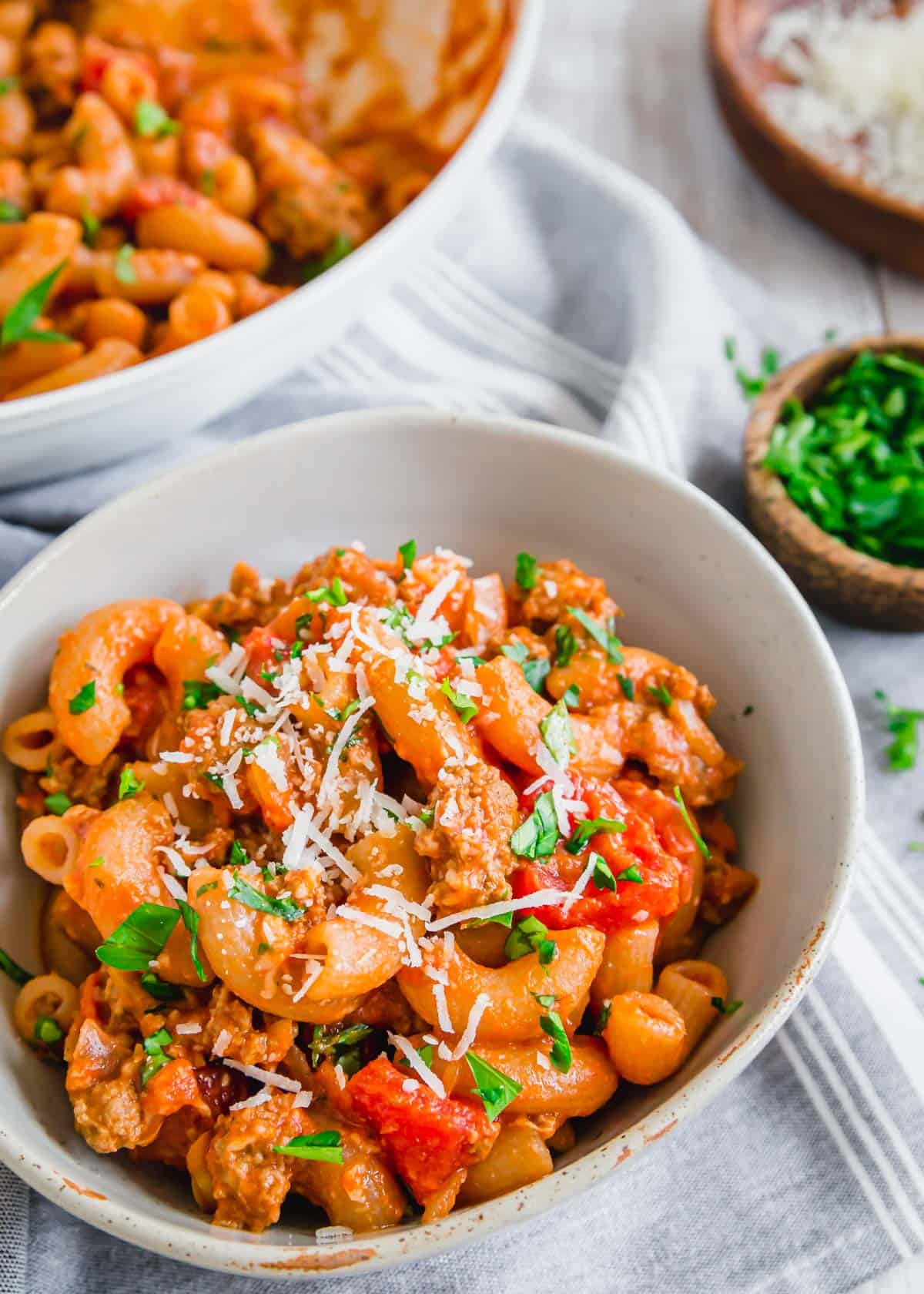 Ground beef with elbow pasta in a tomato sauce with parsley and cheese in a bowl.