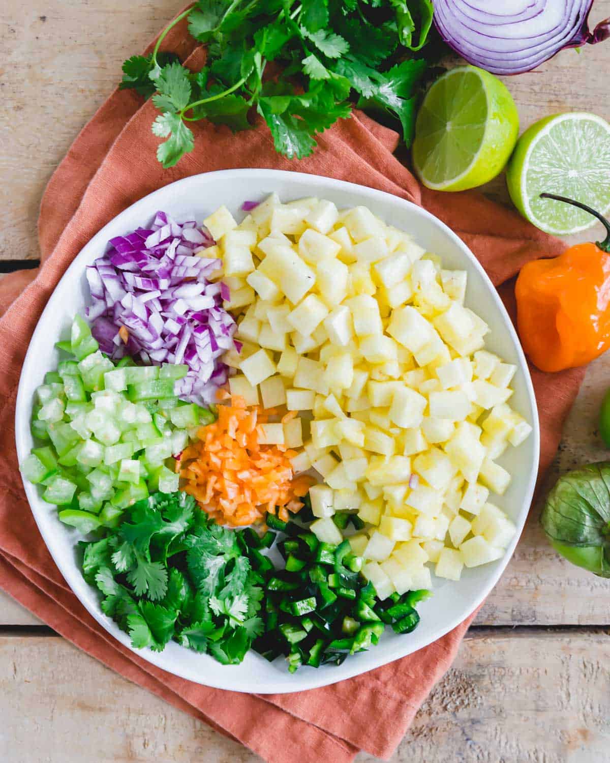Prepped ingredients to make pineapple salsa with habanero pepper on a white plate. Prepped ingredients to make pineapple salsa with habanero pepper on a white plate.