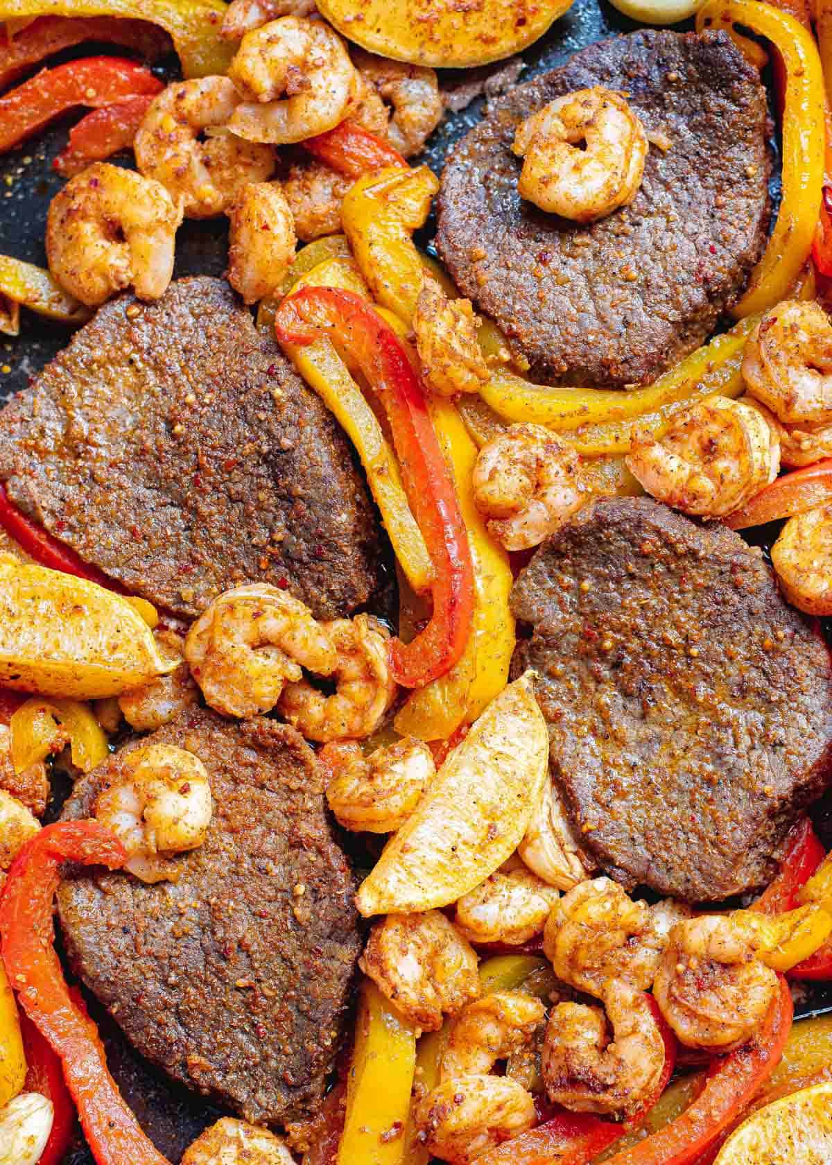 Cooked steak, shrimp, peppers and onions on a sheet pan.