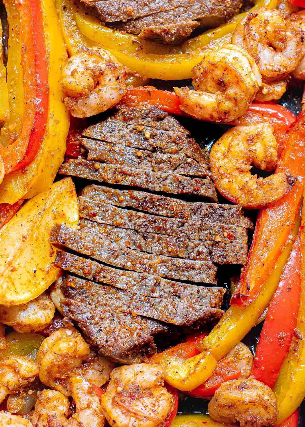 Sliced fajita steak with shrimp, peppers and onions.