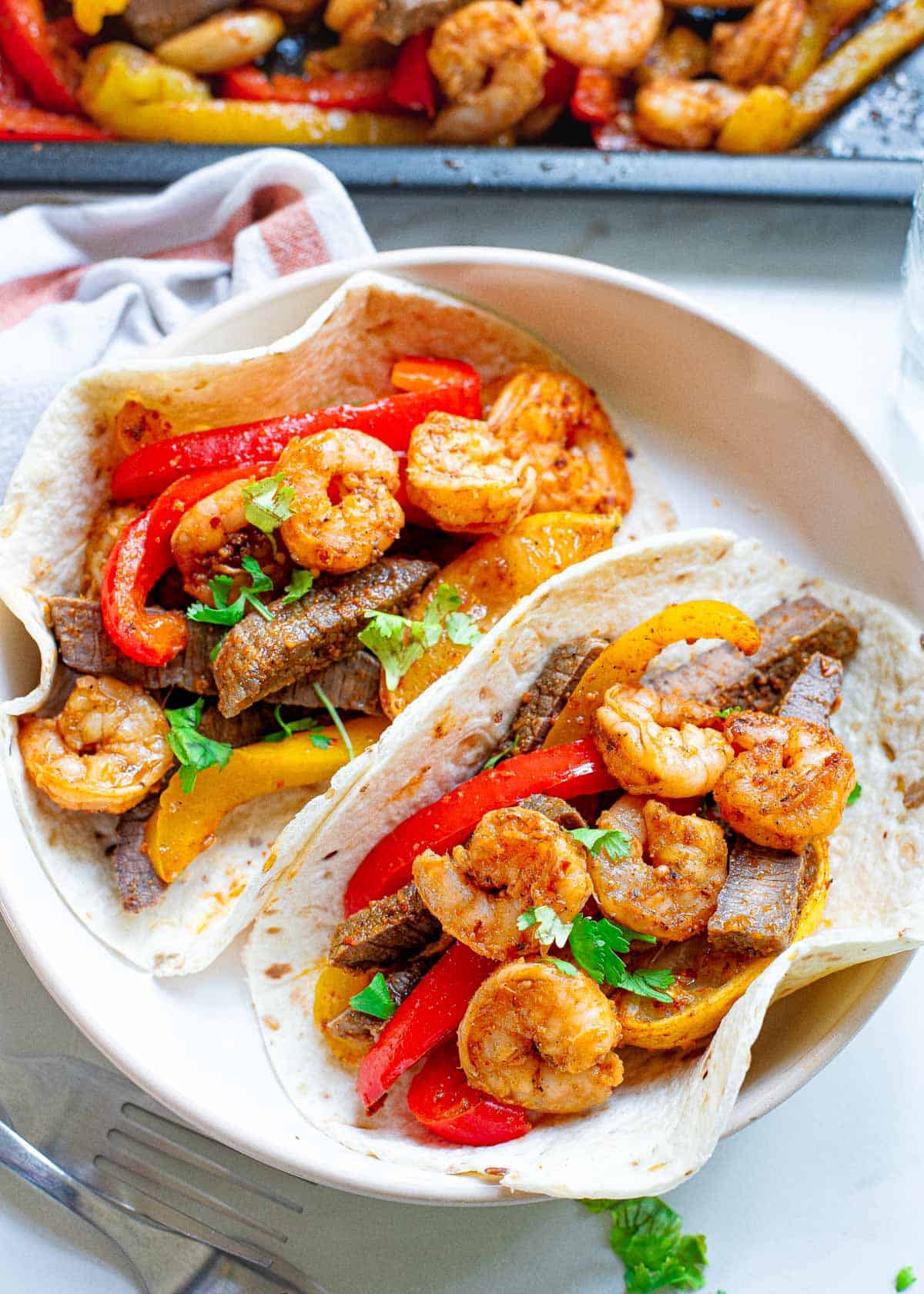 Steak and shrimp fajitas in a flour tortillas on a plate.