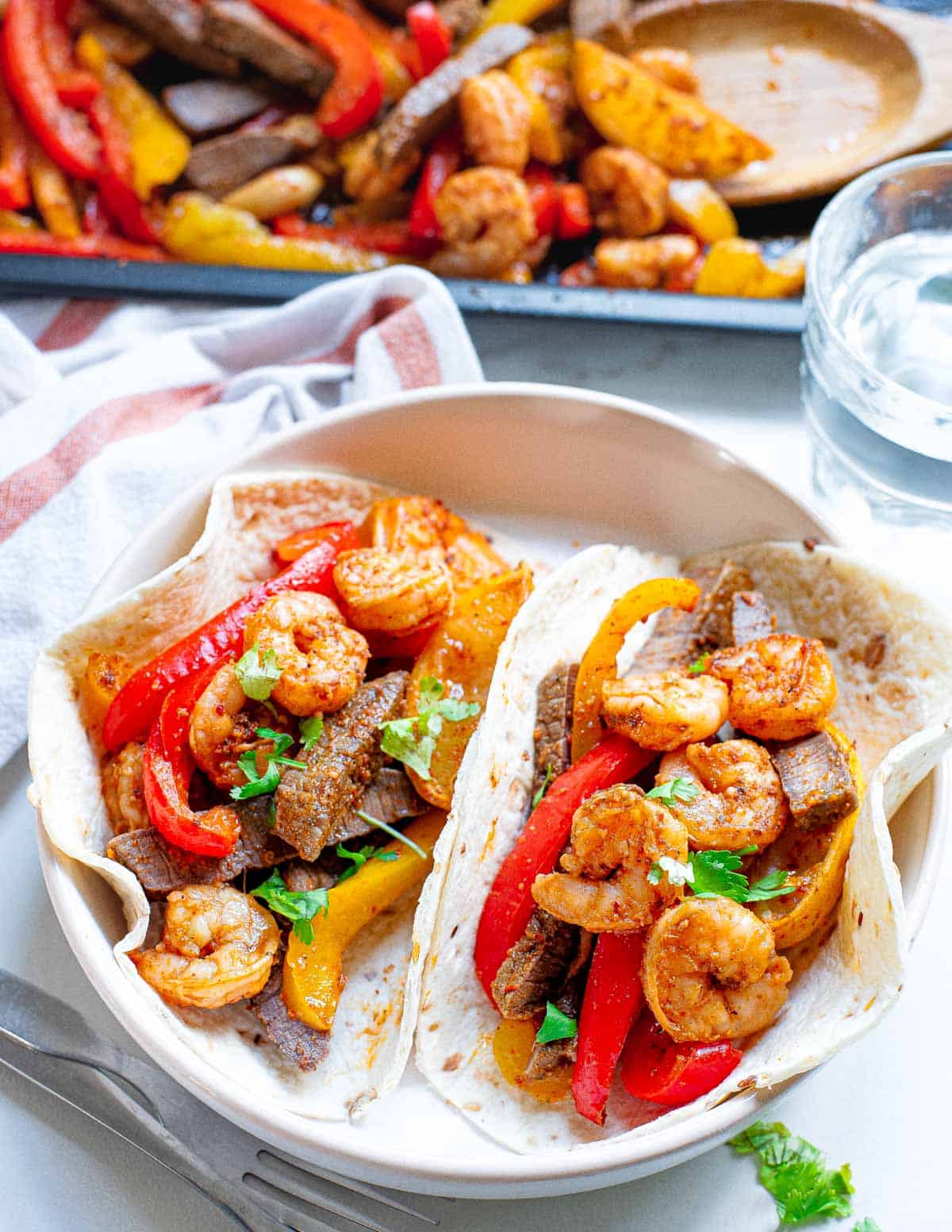 Steak and shrimp fajita recipe served in tortillas on a white plate.