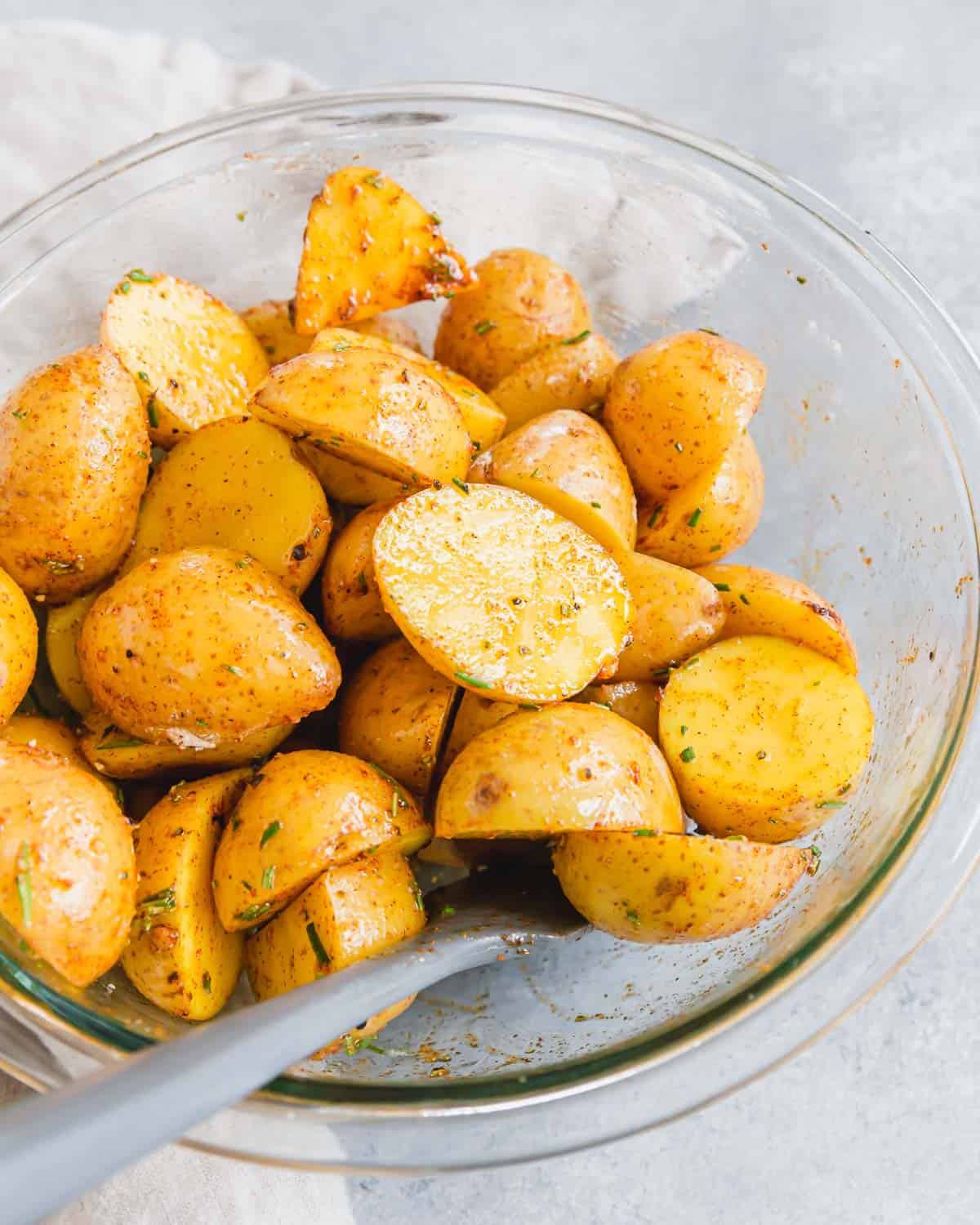 Tossing halved baby potatoes with oil and spices in a glass bowl.