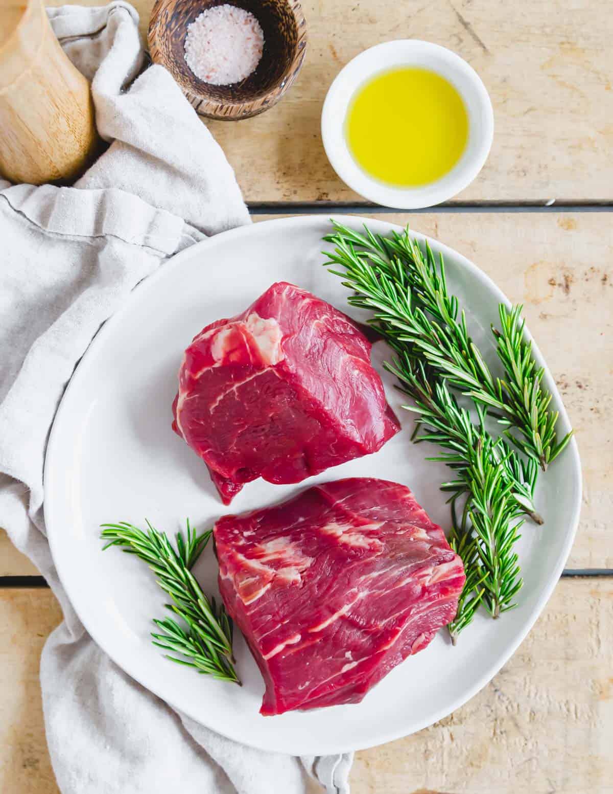 Two pieces of filet mignon on a plate with fresh rosemary.