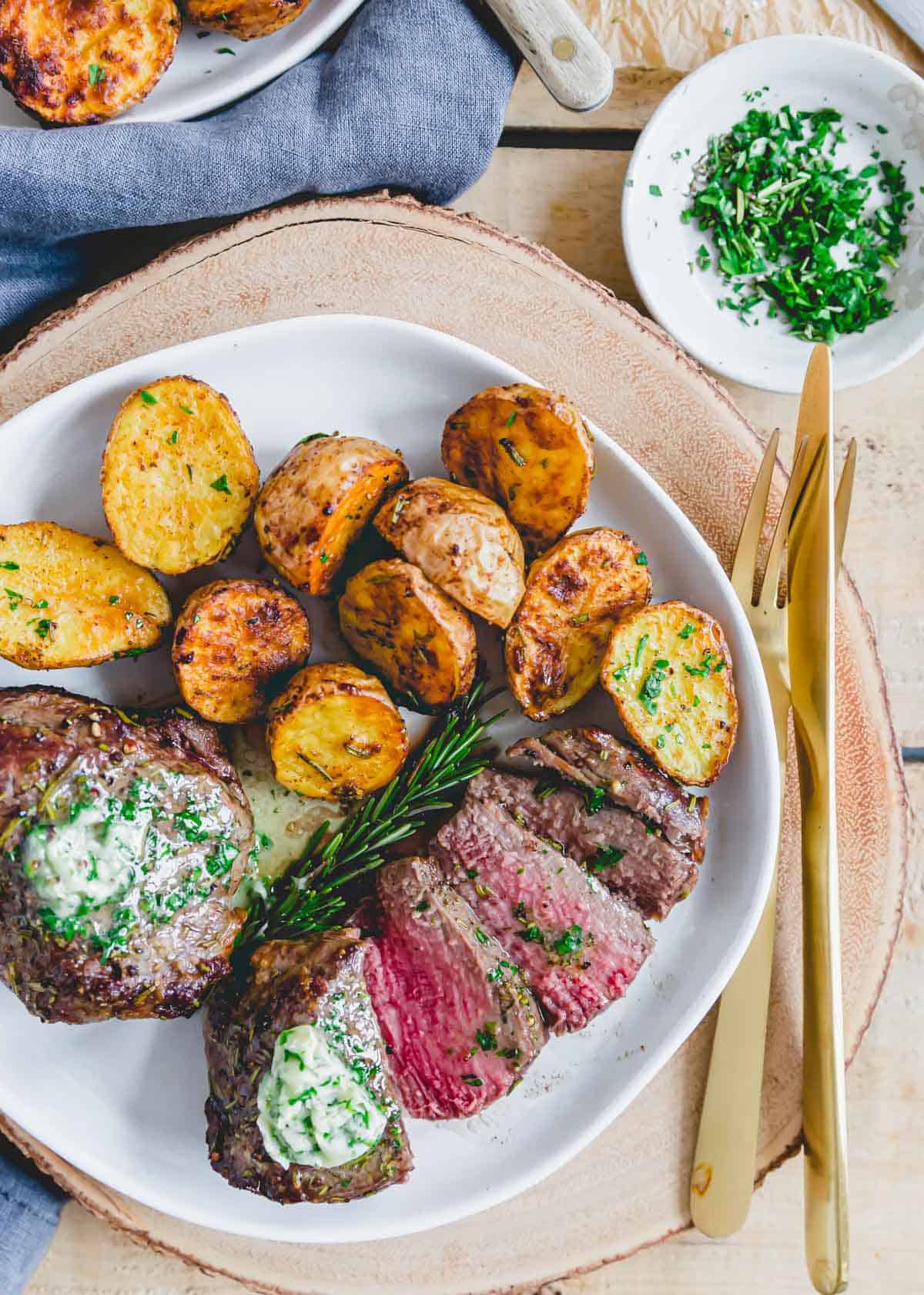 Air fryer filet mignon cooked medium rare sliced on a plate with air fryer roasted baby potatoes.