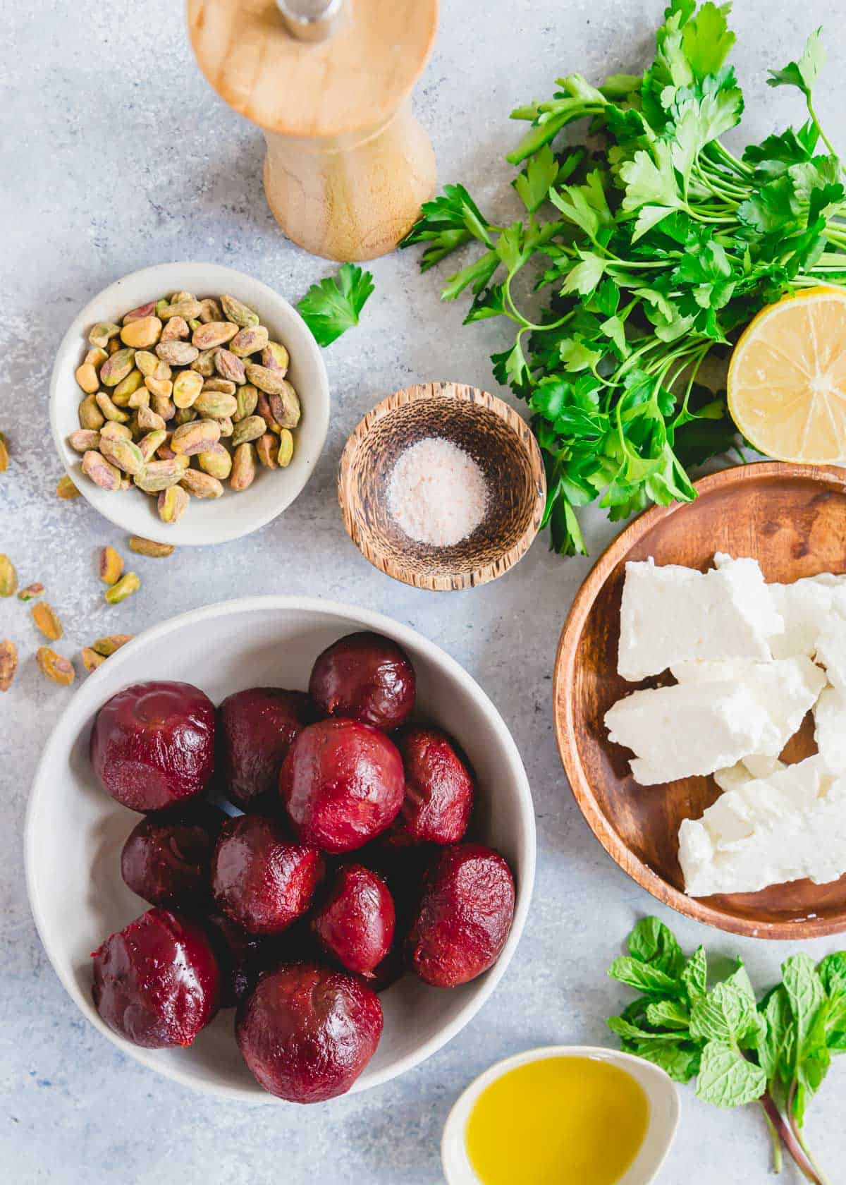 Cooked whole beets, feta cheese, shelled pistachios, parsley and mint in bowls to make a feta beet salad.