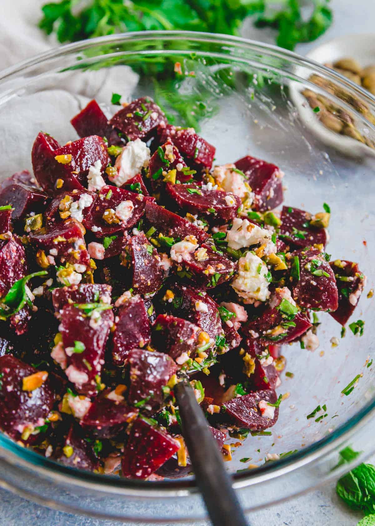 Preparing a salad of beets, feta, pistachios and fresh herbs in a bowl with a spoon.