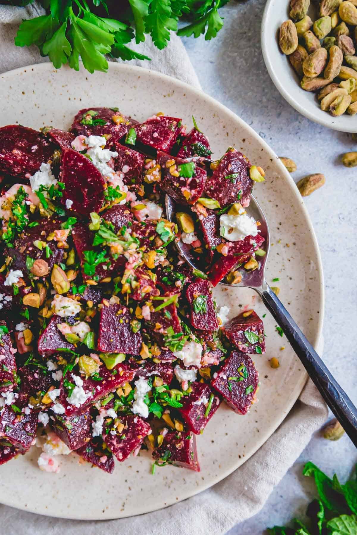 Beet salad with feta, pistachios, fresh herbs and a lemon olive oil dressing on a plate with a black metal spoon.